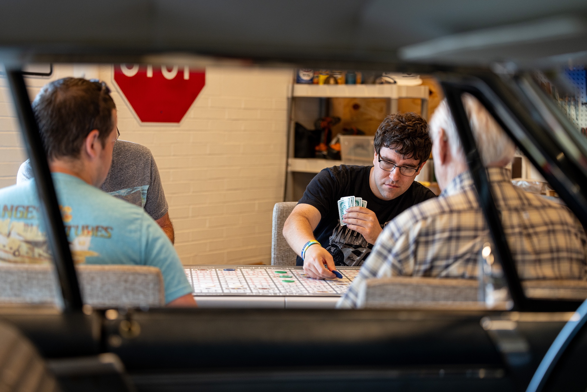 A group of people play a game of Sequence. The shot is framed through an antique car window.