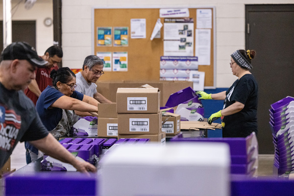 A long table with people packing boxes with products