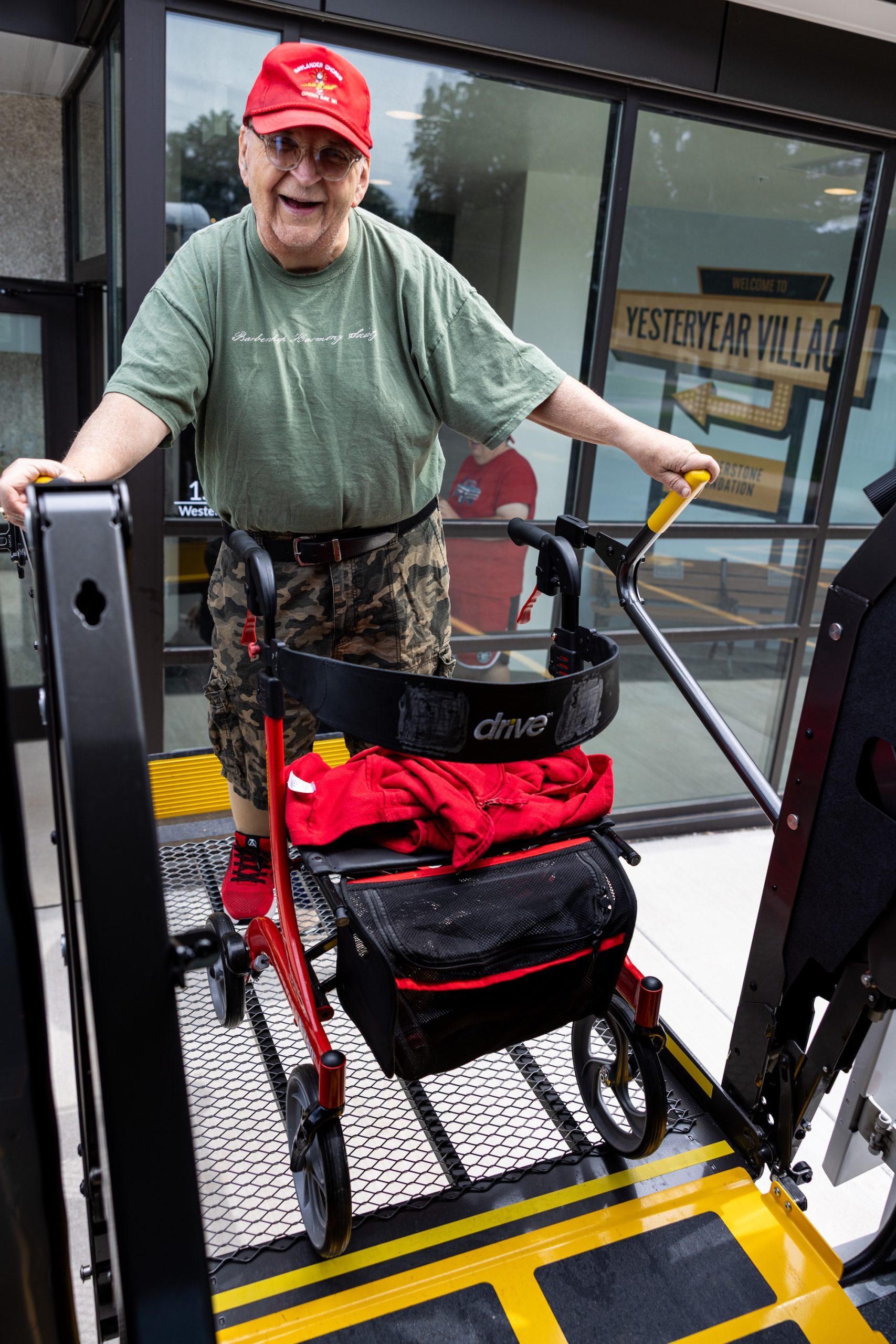 An elderly man with a walker happily rides up a ramp to board a Curative Connections bus.