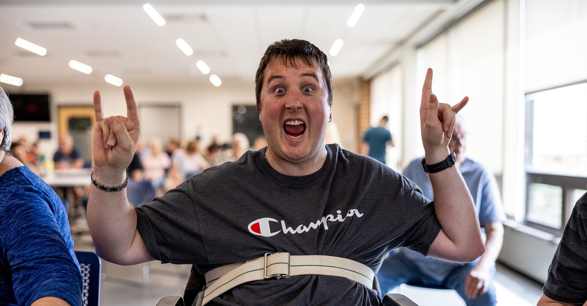 A man in a wheelchair shows his enjoyment to music by showing the camera rock 'n roll horns with his hands.