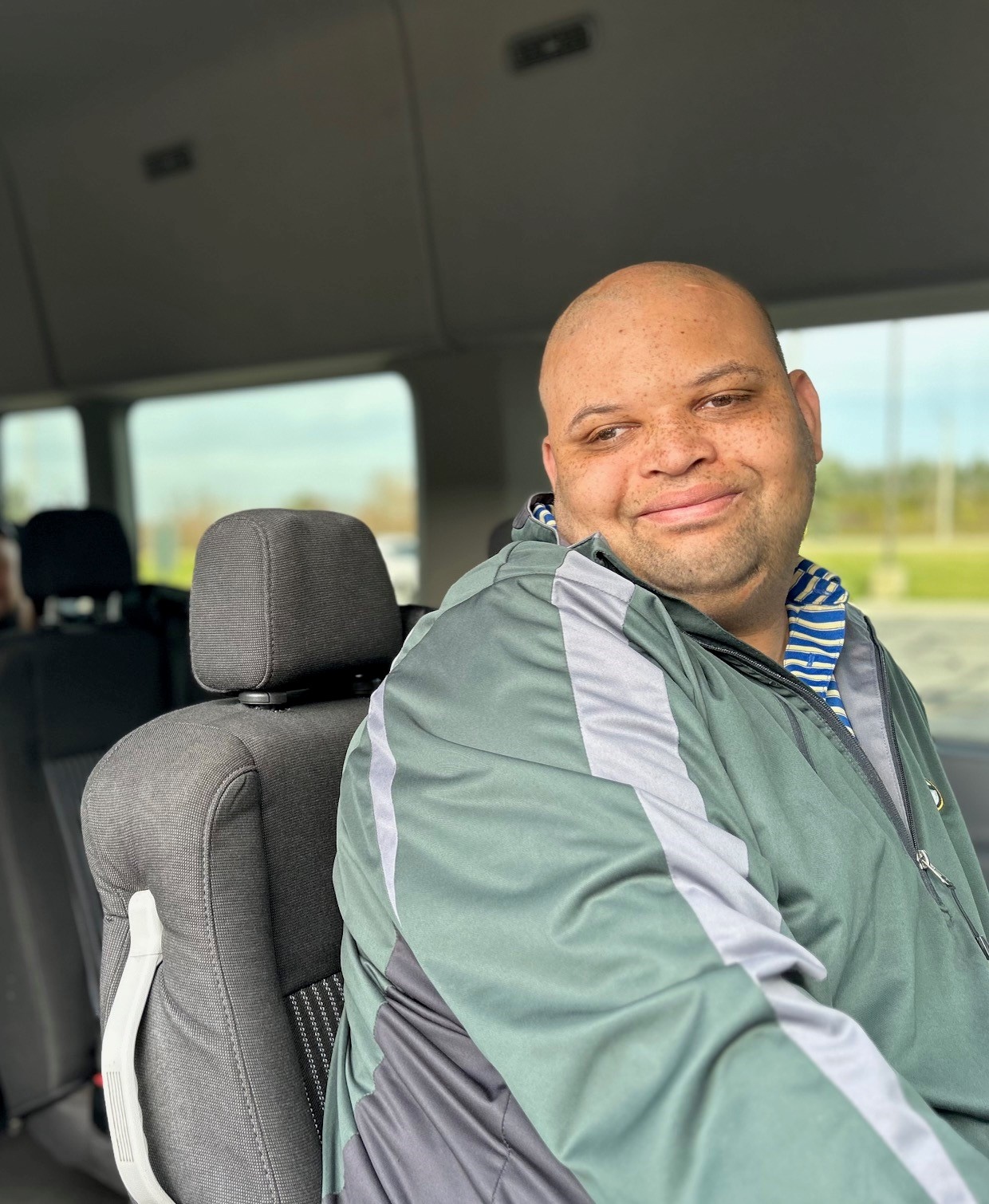 A bald man in a green track suit smiles at the camera as he rides a Curative Connections bus.