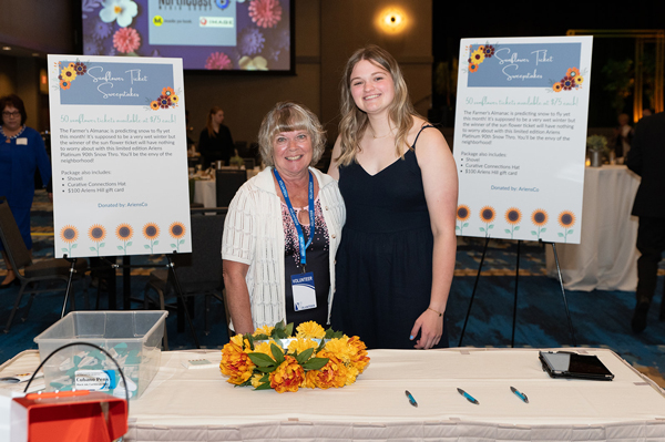 Two women posing together in front of a welcome table with poster boards behind them