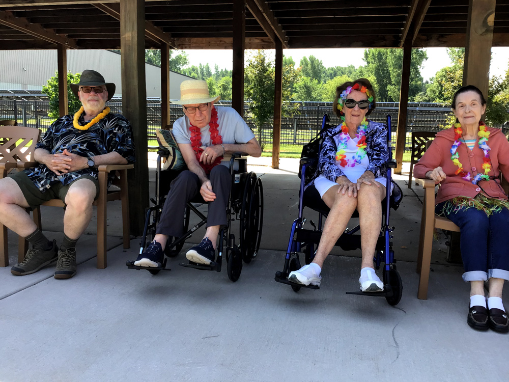 Four elderly people sitting outdoors in a row, the middle two are sitting in wheelchairs