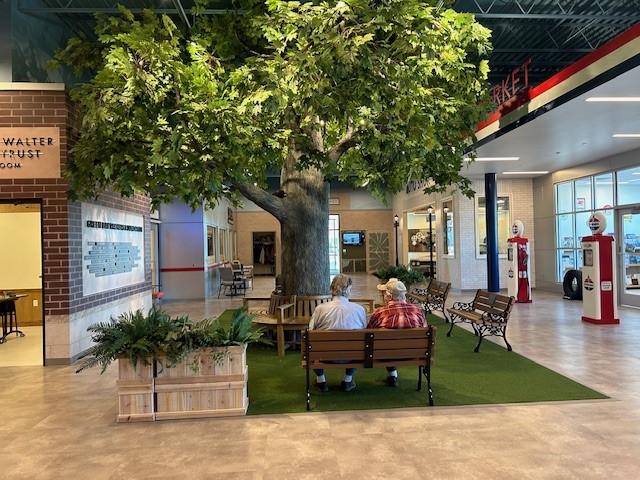 Two men sitting on a bench beneath a fake tree that's indoors