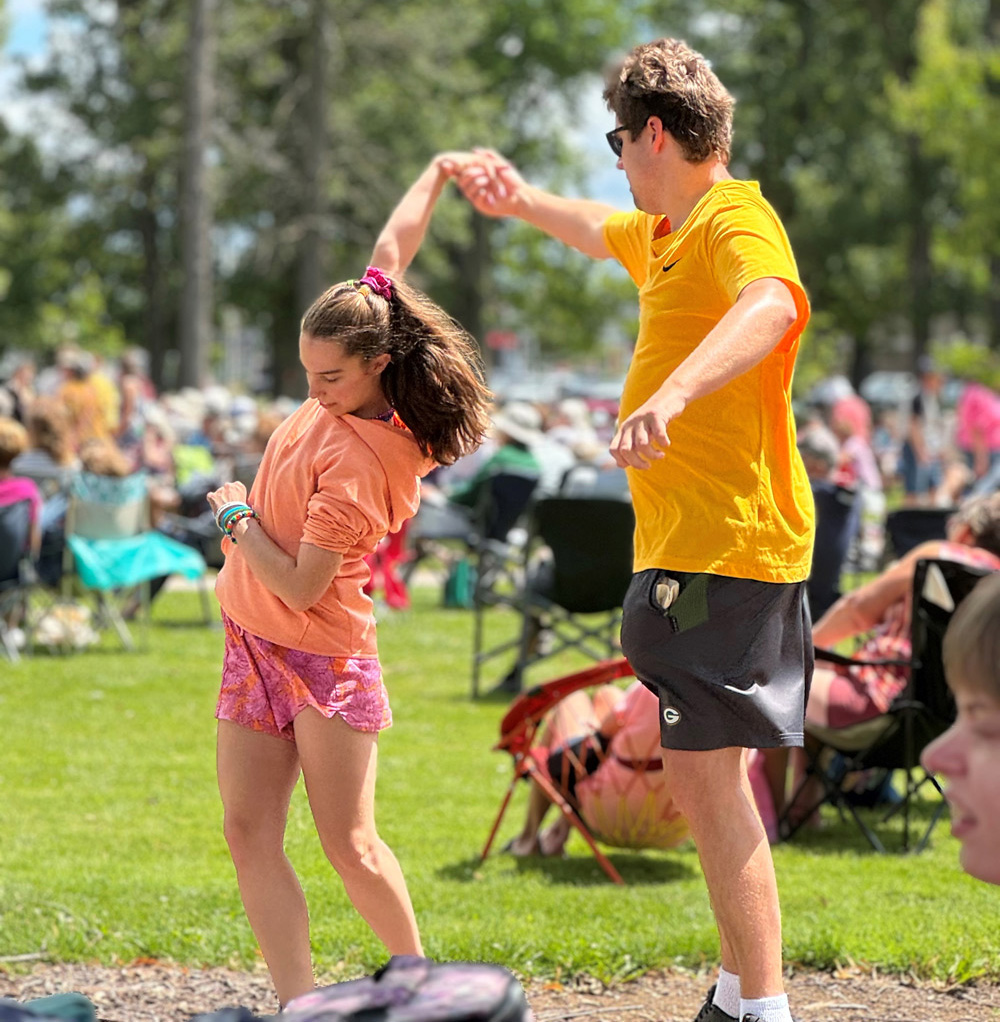 A man dancing with a young girl in a park with lots of people