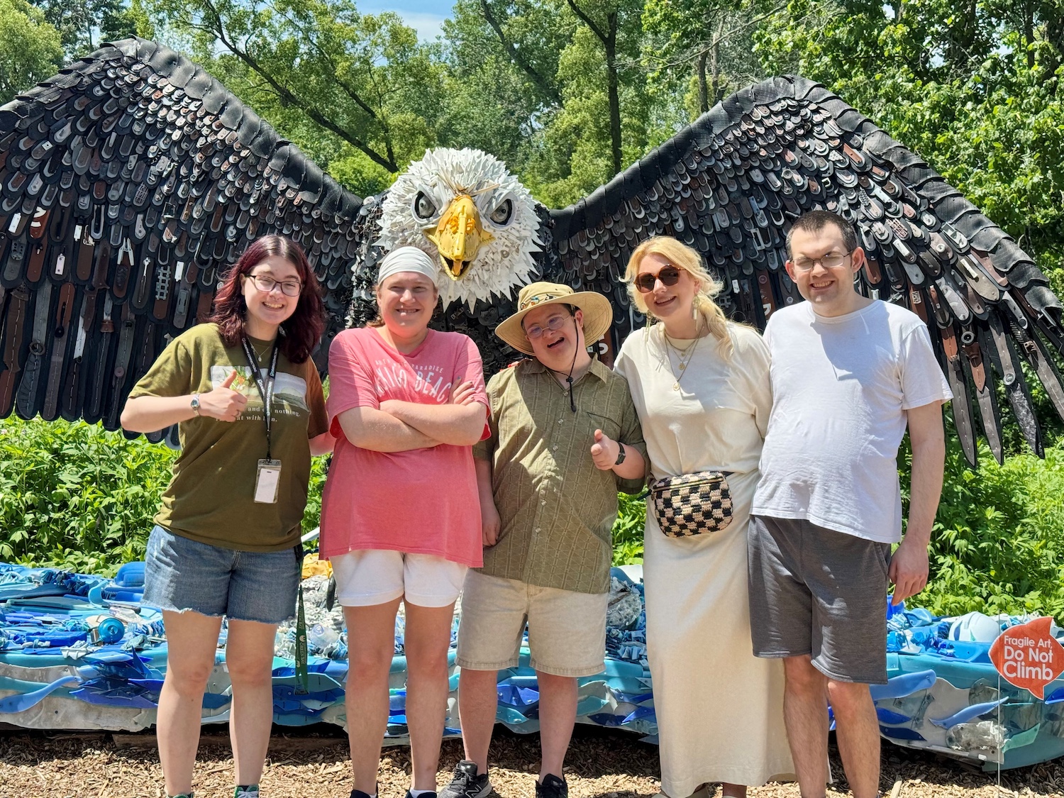 A group of Cognitive Rehab and Wellness participants pose in front of a big sculpture eagle at a park.