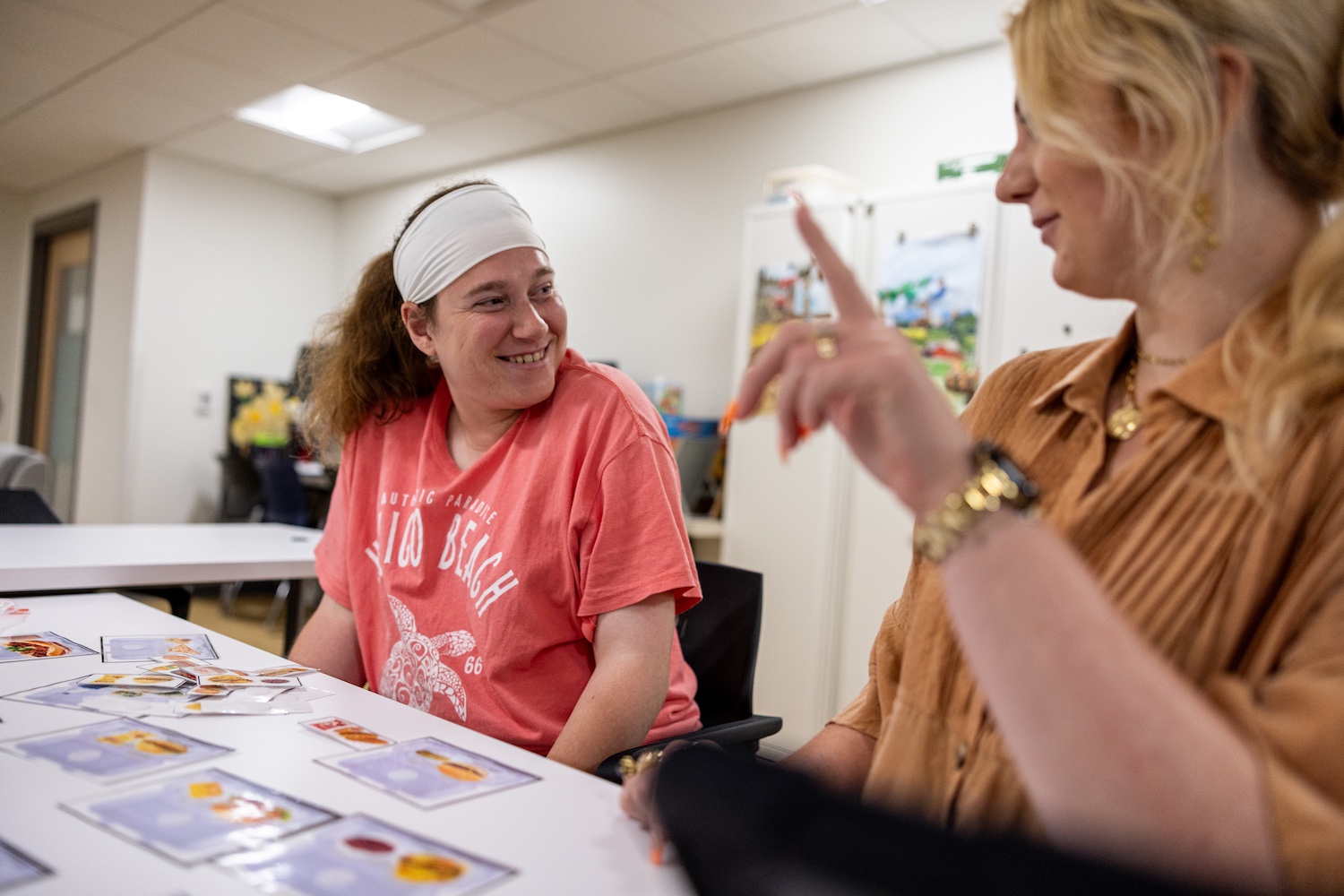A woman in a pink shirt smiles at another woman during a Cognitive Rehab and Wellness program at Curative Connections.