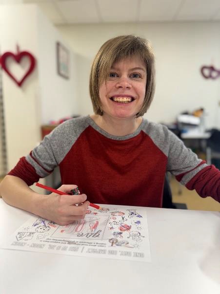 A woman in a red and gray shirt smiles for the camera as she works on a worksheet.