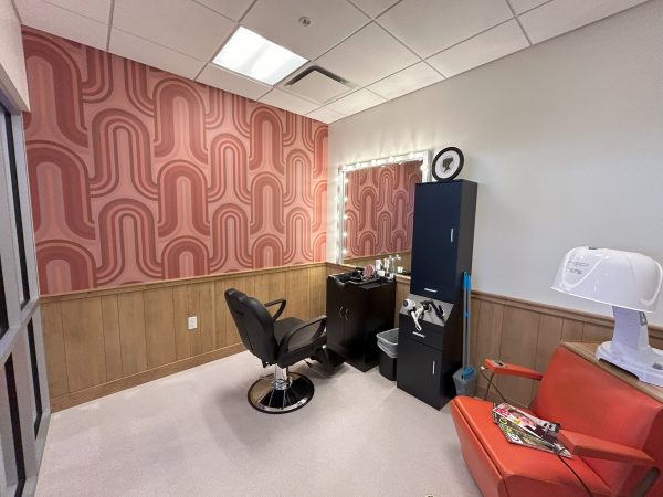 The interior of the Yesteryear Village salon and barbershop. The walls have red funky wallpaper and the there is a salon chair and sink.